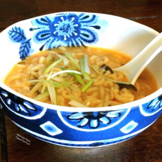 Ramen soup in a decorative blue and white bowl. The ramen is garnished with slivered scallions.
