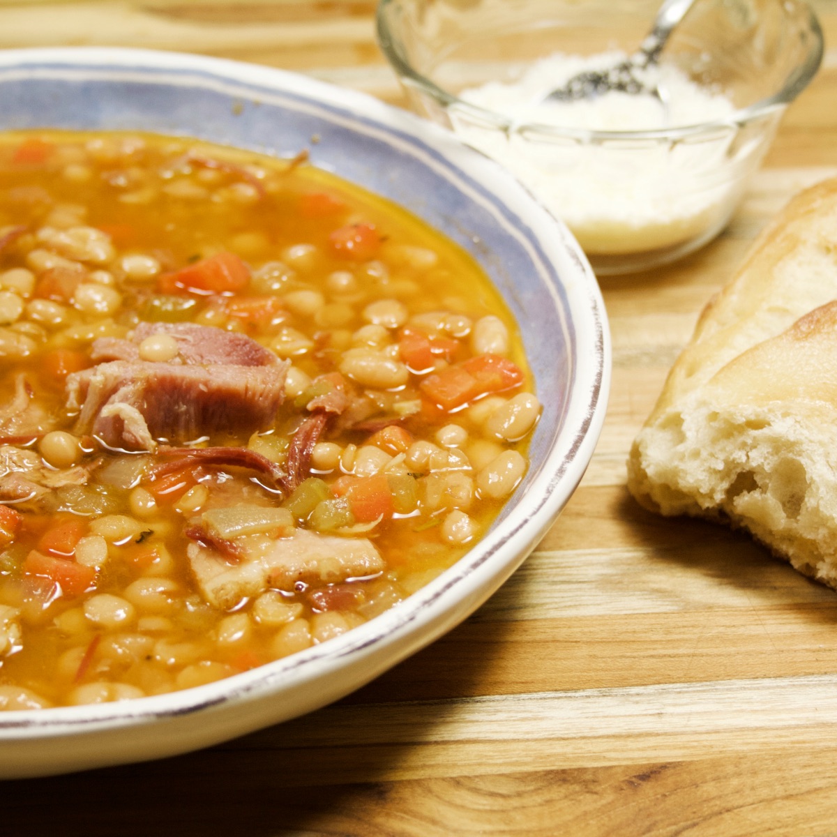 Close-up of Instant Pot Ham and Bean Soup in a blue and white bowl next to a hunk of crusty bread.