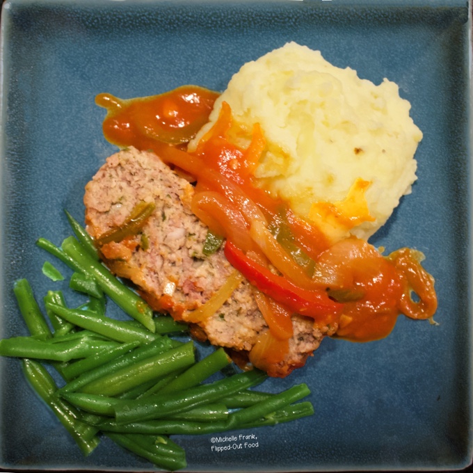 Top view of a serving of Mediterranean-Style Meatloaf topped with the pepper sauce on a blue plate with sides of green beans and mashed potatoes.