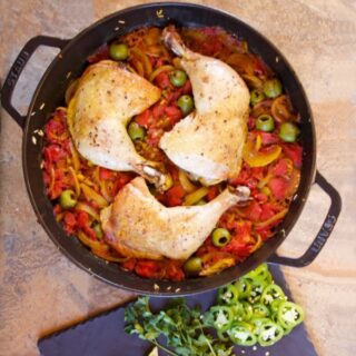 One-Pan Arroz con Pollo: the finished chicken in the skillet with the rice. A slate-grey platter of garnishes sits next to the skillet.