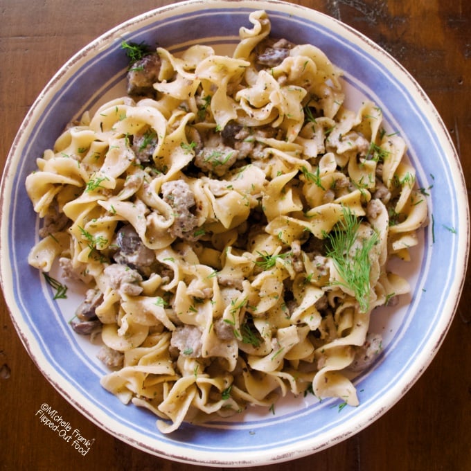 A serving of One-Pot Ground Beef Stroganoff in a blue and white bowl with a sprig of dill on top.