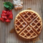 Beautiful waffle on striped plate with mint, strawberries, and whipped cream