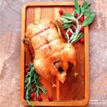 herbed roast duck on a platter with fresh herbs and cranberries