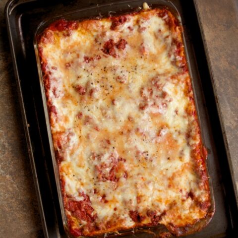 Lasagna Bolognese in a baking dish set upon a baking sheet. The lasagna is straight out of the oven and piping hot.