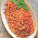 Slow-roasted tomato sauce served over spaghetti on a decorative platter with a sprig of basil.