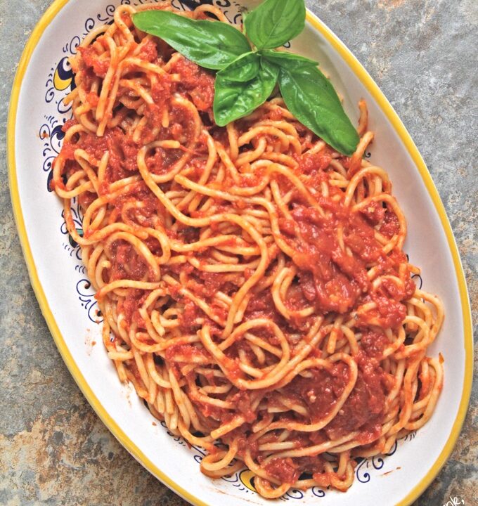 Slow-roasted tomato sauce served over spaghetti on a decorative platter with a sprig of basil.