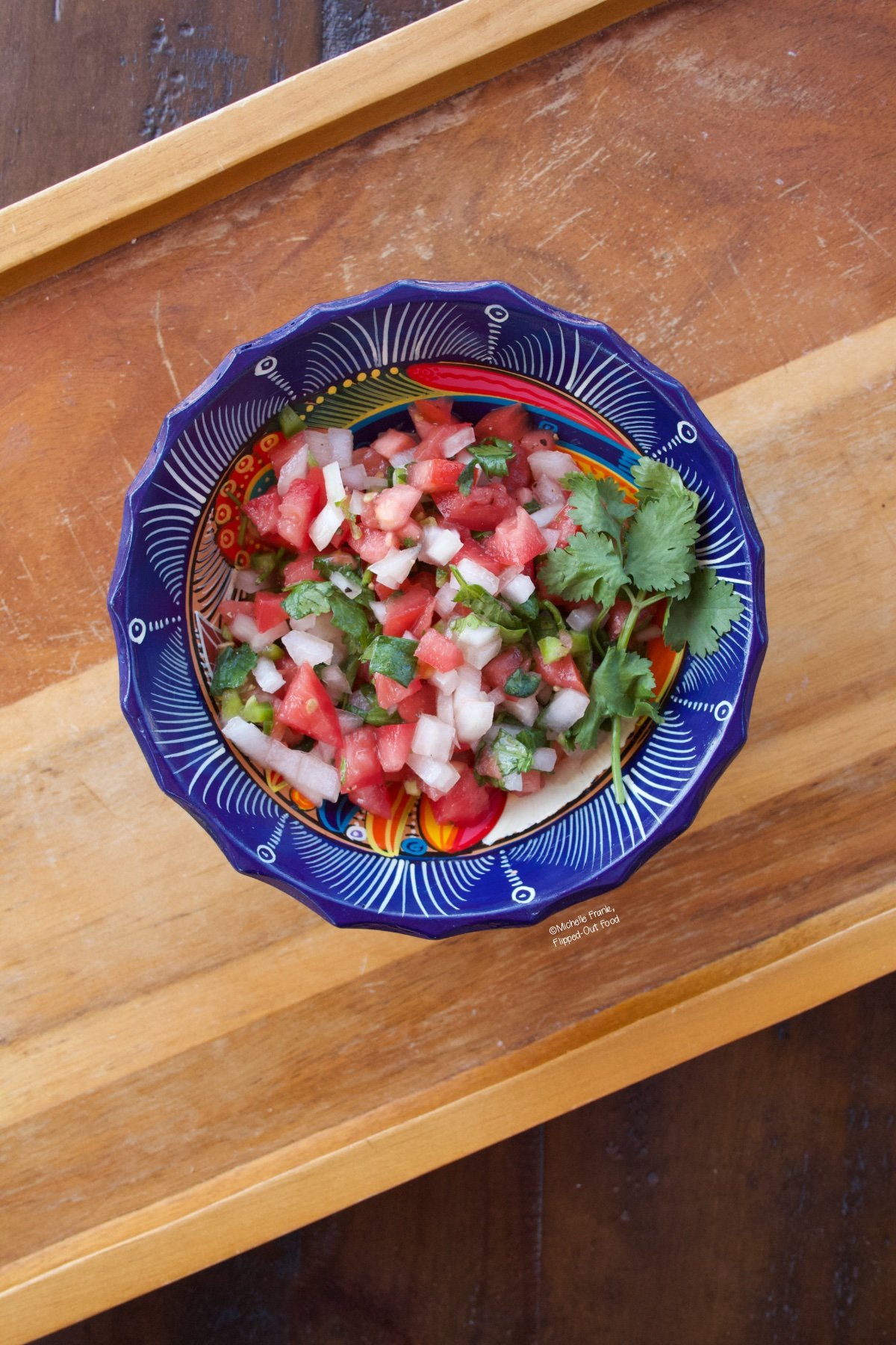 Pico de gallo in a decorative blue bowl sitting atop a wooden tray.