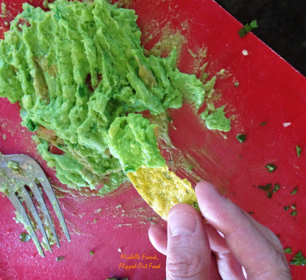 Top view of tortilla chip loaded with fresh guacamole above a red cutting board.