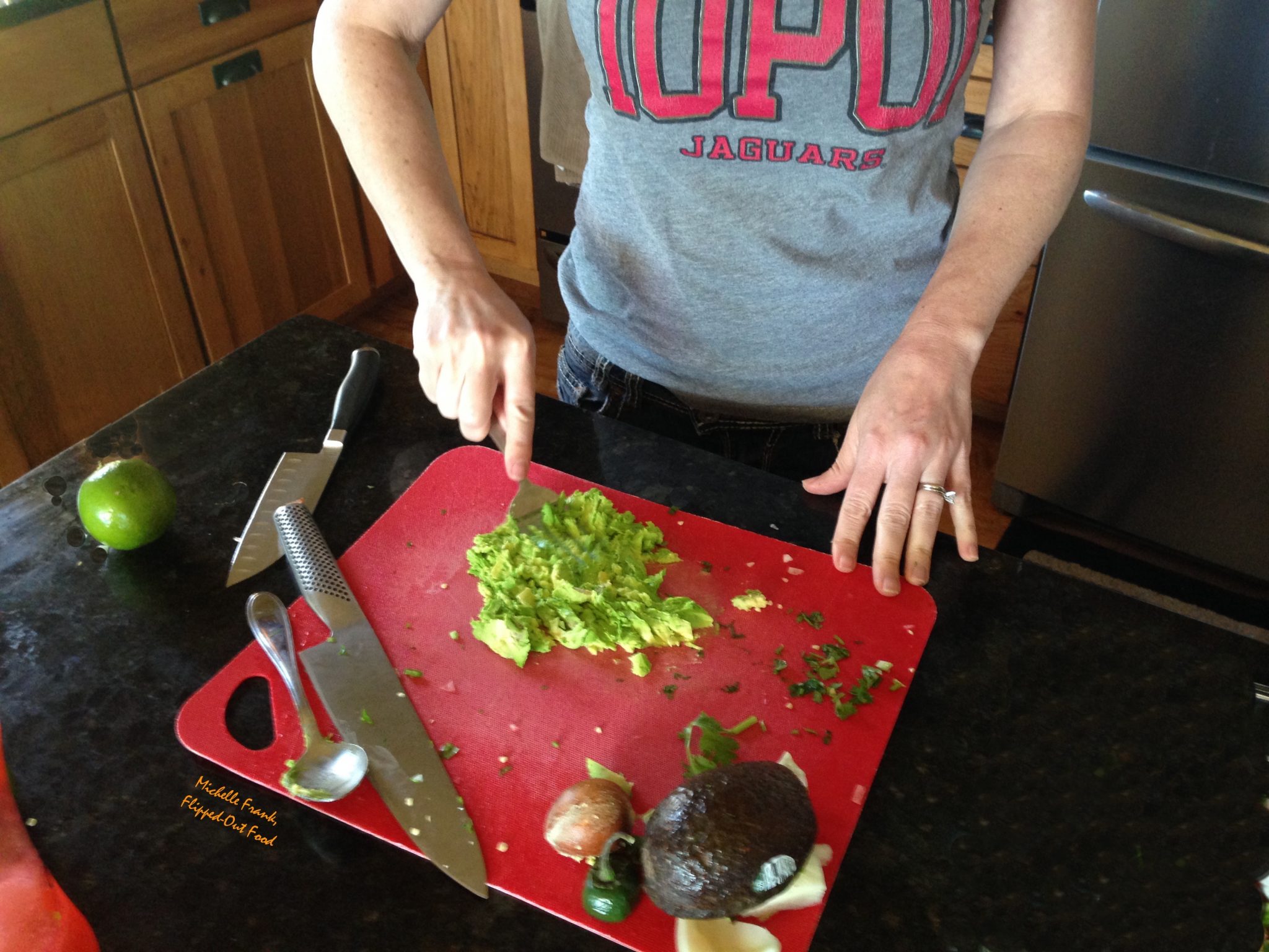 A fork mashing up avocados with a large fork on a red cutting board.