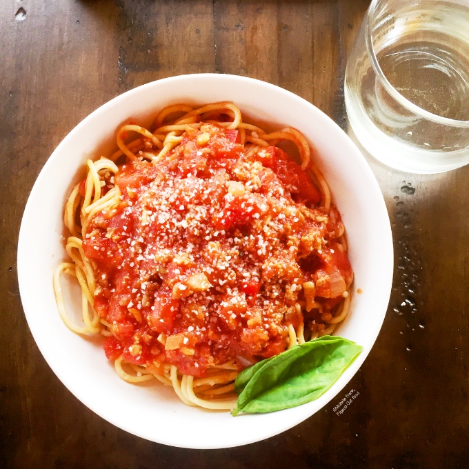 Easy Cheat Bolognese Sauce, garnished with basil leaves and Parmesan cheese.