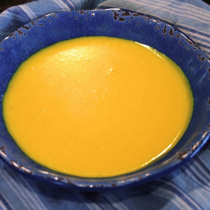 Ginger-Turmeric Butternut Squash soup is a beautiful bright yellow, set of by a blue bowl.