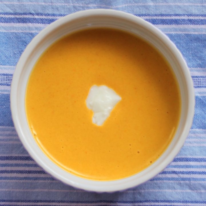 Overhead of curried acorn squash soup in a white bowl set atop a blue and white striped cloth.