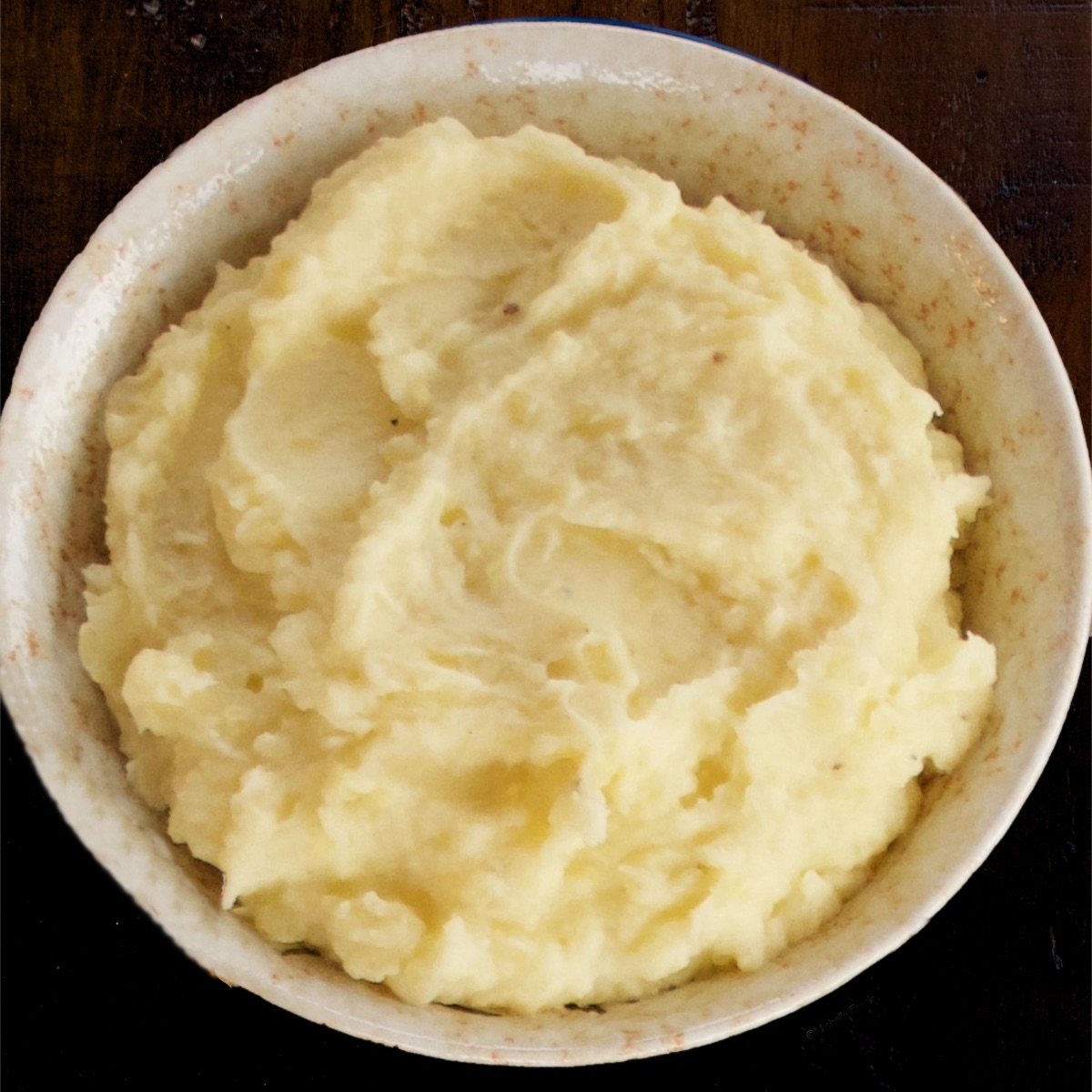 Meal-Prep Creamy Mashed Potatoes in a ceramic bowl set on a dark, wooden table.