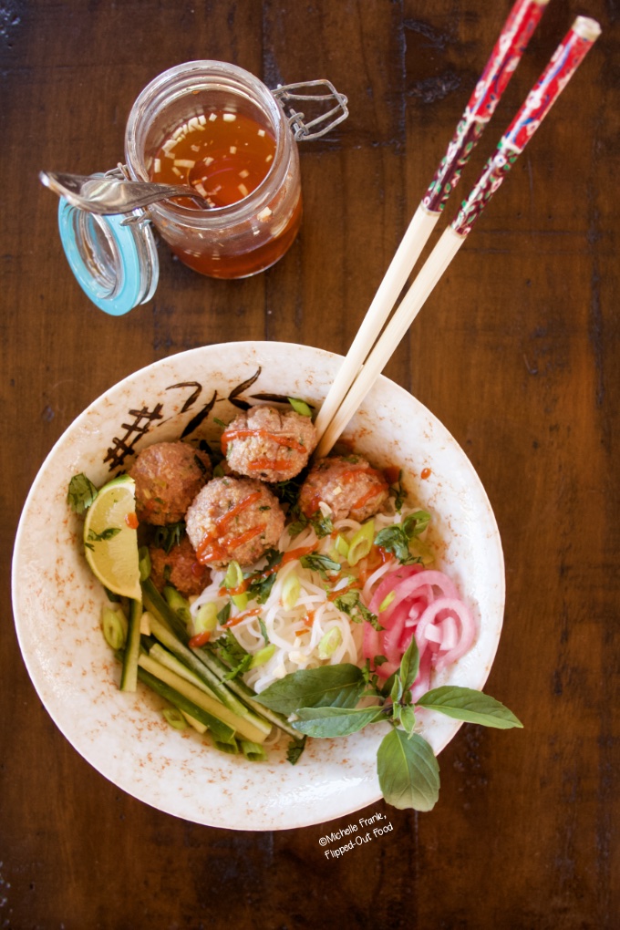 Overhead view of a serving of Bun Cha Vietnamese meatball noodle bowls, garnished with Thai basil and pickled red onion, with chopsticks and a jar of nuoc cham.