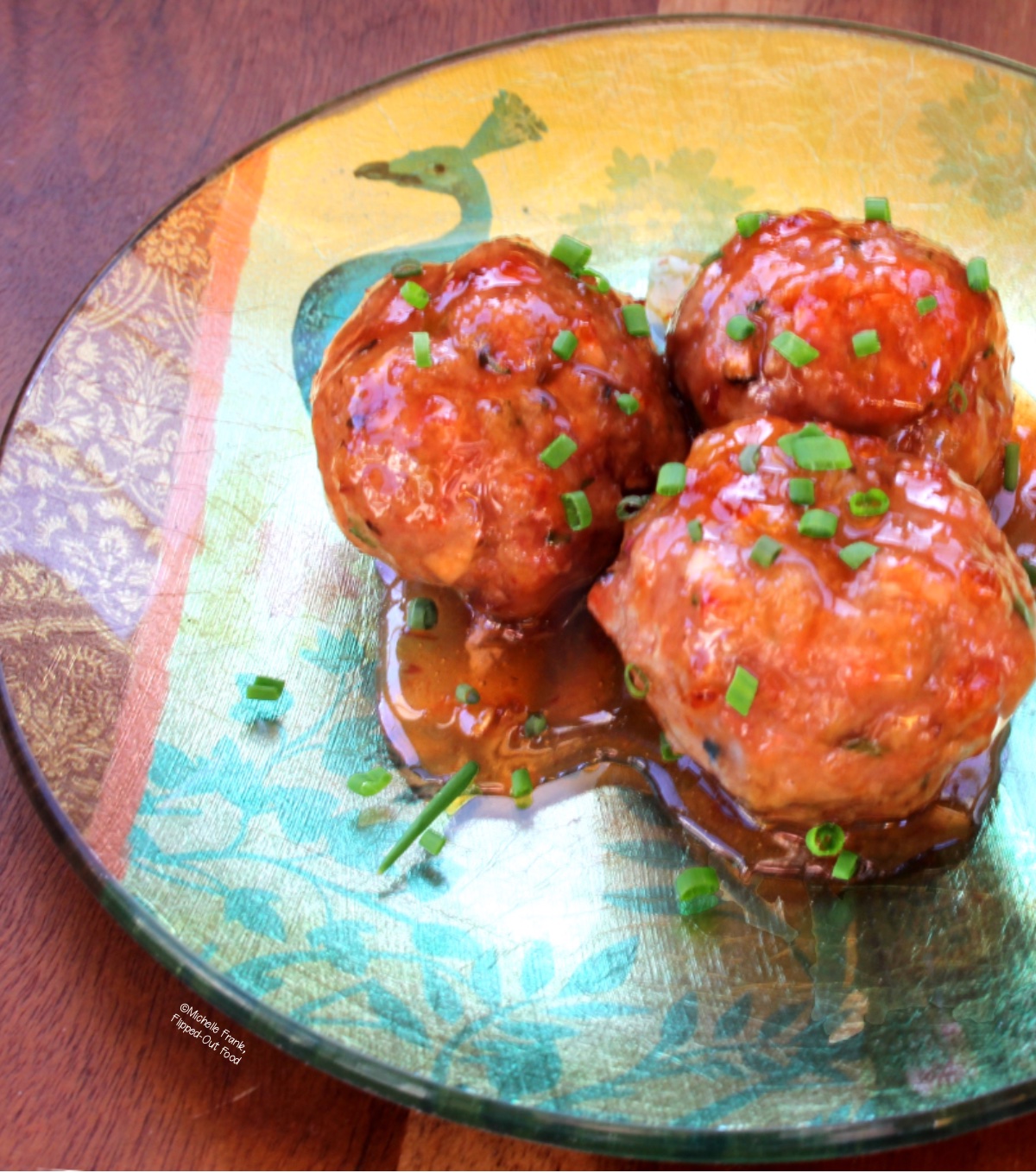 Three Asian meatballs on a decorative party plate. The meatballs are garnished with minced chives.