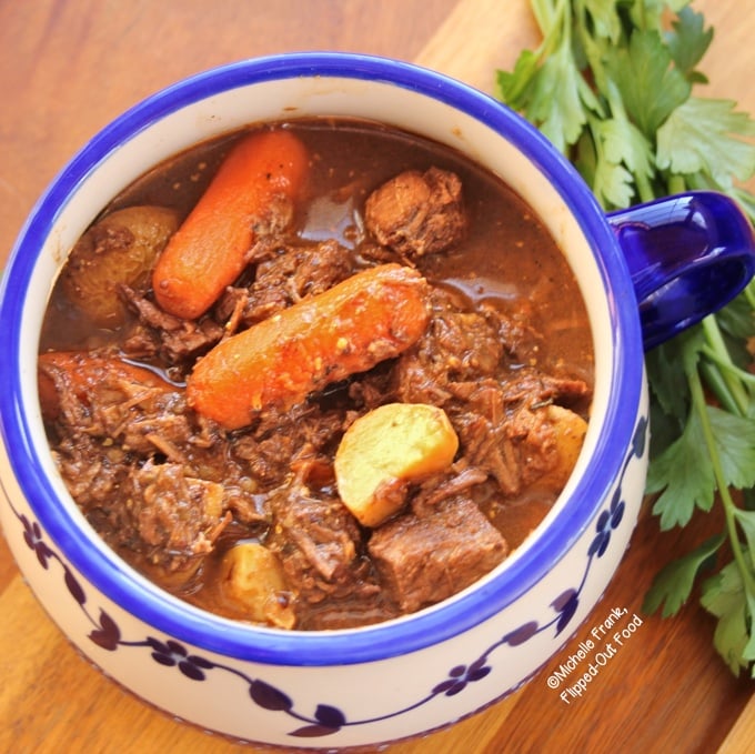 A side-view of Irish Guinness Stew in a one-handled blue and white bowl sitting next to a bunch of parsley.