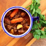 A heaping serving of Make-Ahead Irish Guinness Stew in a one-handled blue and white bowl. The stew is loaded with carrots, potatoes, and fall-apart tender meat. The rich, complex broth is the result of beef slowly simmering in Guinness Stout, along with a few other flavor-building hacks. |Irish Food | Comfort Food | Guinness Stew | Beef Stew | Lamb Stew