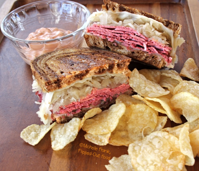 Side view of Best-Ever Reuben Sandwiches served with 1000 island dressing on the side in a clear ramekin and a serving of chips. #reubensandwich #saintpatricksday #stpaddysday #cornedbeef #pubfood #sandwich via @flippedoutfood