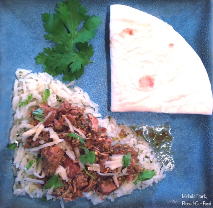 Easy Slow-Cooker Pork Salsa Verde (Green Chile Pork), served over rice on a blue plate with a folded flour tortilla and lots of chopped cilantro.