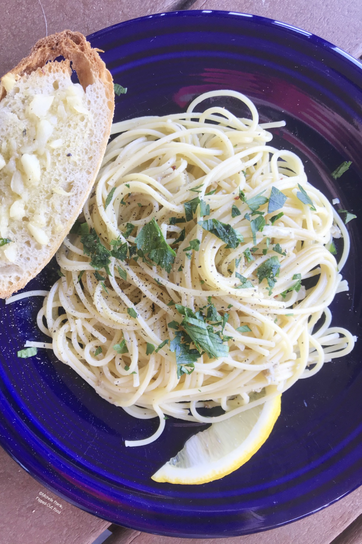 A serving of Pantry Linguine with Clam Sauce, garnished with parsley, on a blue plate next to a slice of toasted bread that has been smeared with roasted garlic.