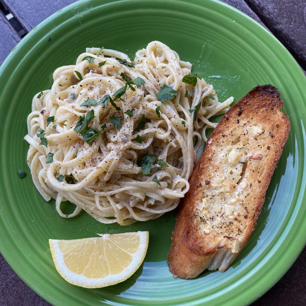 Pantry Linguine with Clam Sauce garnished with parsley, on a green plate with a toasted slice of garlic bread and a lemon wedge.