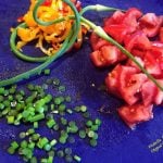 Garlic Scapes, whole and sliced, on a cutting board with tomatoes and sliced yellow sweet peppers. Great in Garlic Scapes Pesto and Garlic Scapes Vinaigrette Dressing. #seasonalingredients #garlicscapes #seasonalfood #healthyfood #healthyeating #flippedoutfood @FlippedOutFood