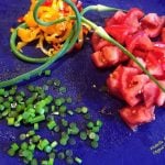 Garlic Scapes, whole and sliced, on a cutting board with tomatoes and sliced yellow sweet peppers. Great in Garlic Scapes Pesto and Garlic Scapes Vinaigrette Dressing. #seasonalingredients #garlicscapes #seasonalfood #healthyfood #healthyeating #flippedoutfood @FlippedOutFood