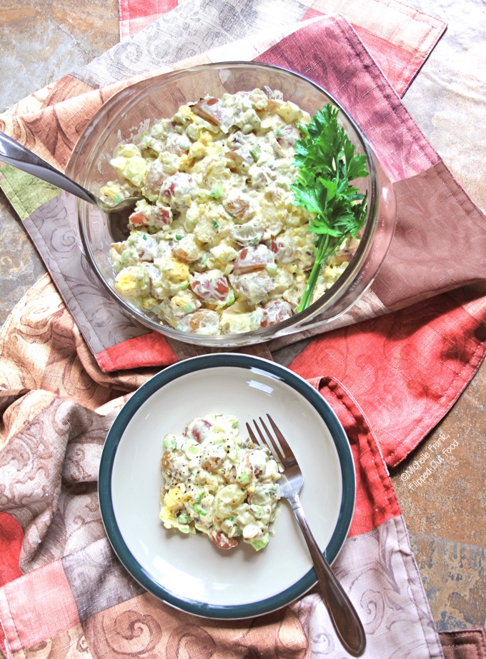 Bowl of classic potato salad in clear bowl with a serving of it on a plate next to the bowl.