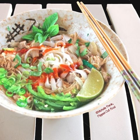 Slow-cooker Rotisserie Chicken Pho Ga, side view of a bowl loaded up with herbs, jalapenos, scallions, and sriracha. #vietnamesefood #phoga #pho #phonoodlesoup #vietnamesechickennoodlesoup @FlippedOutFood