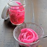 Easy Pickled Red Onion in a serving dish and storage jar, sitting on a rustic table. A must-have garnish for a variety of dishes, from Mexican to Asian and everything in between! #garnish #relish #condiment #pickledredonion #flippedoutfood @FlippedOutFood