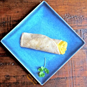 Green Chile Frittata Wraps: top view of a wrap set onto a square, blue plate with a sprig of cilantro.