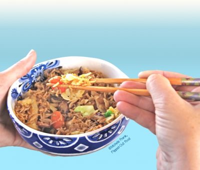 Eating leftover vegetable fried rice with chopsticks. A view of the rice in a blue bowl being held in one hand with a loaded-up pair of chopsticks in the other hand. 