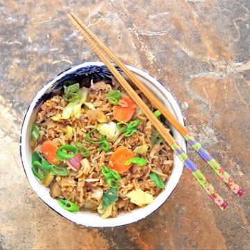 Overhead shot of leftover vegetable fried rice in a blue and white bowl with a pair of chopsticks on top.