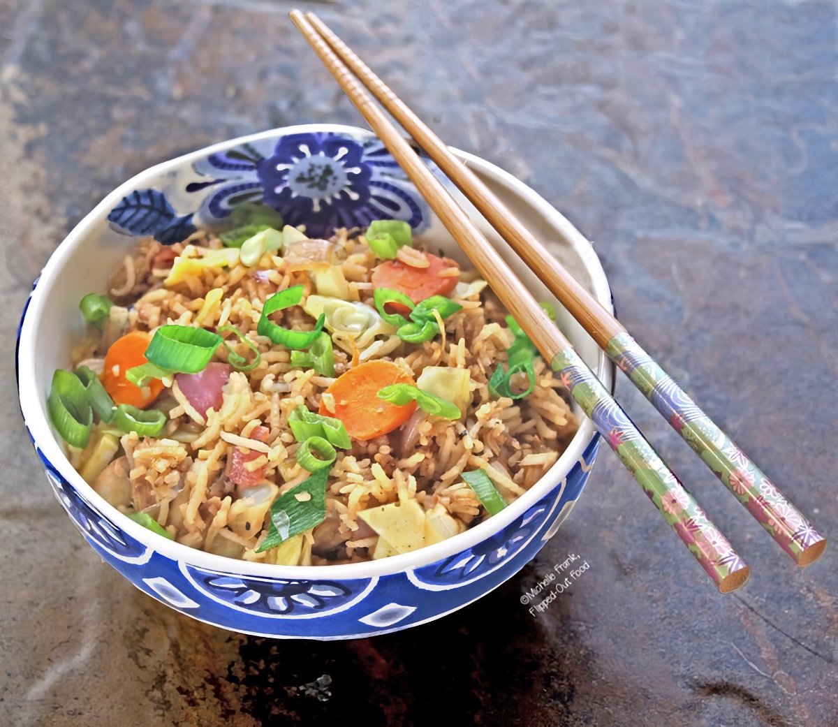 Leftover Vegetable Fried Rice in a blue and white ceramic bowl with a pair of chopsticks laying on top.