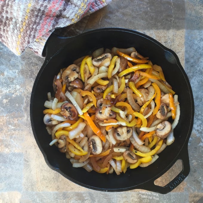 Overhead view of Mushroom-Onion-Pepper Stir-Fry in cast-iron skillet with a towel wrapped around the handle.