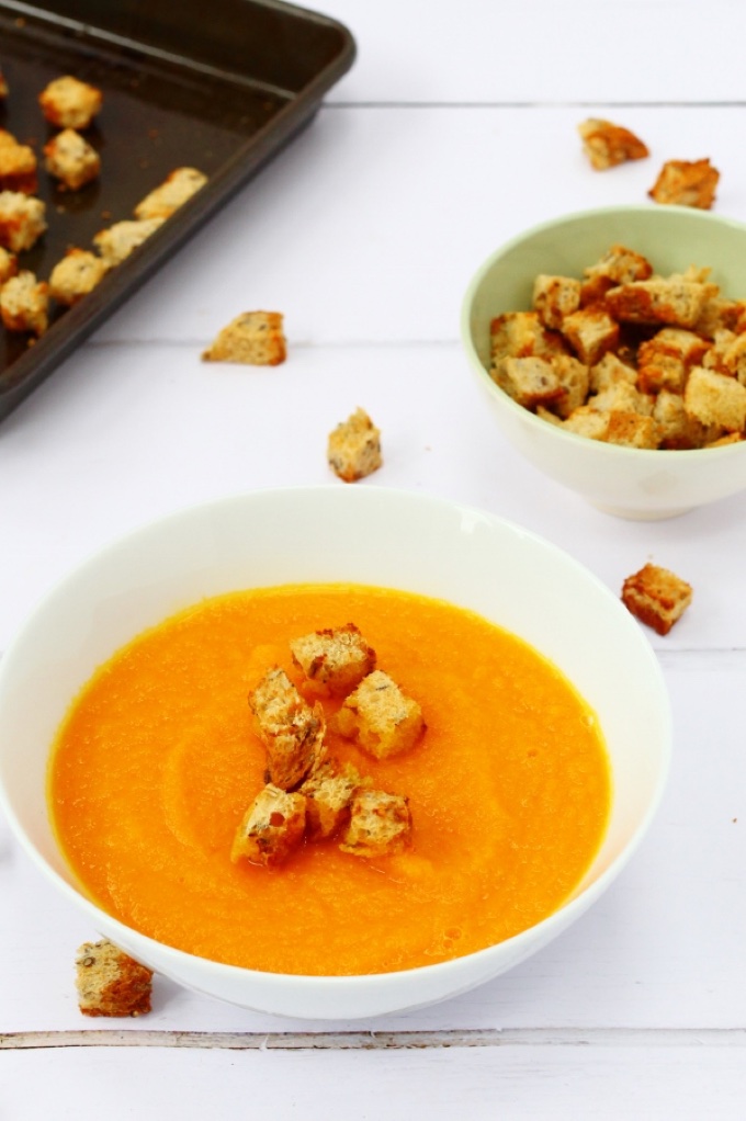 4 main dishes under 45: 1. A bowl of vibrant carrot and ginger soup with Marmite croutons. A few of the croutons are scattered on the table and a bowl of croutons sits in the background.