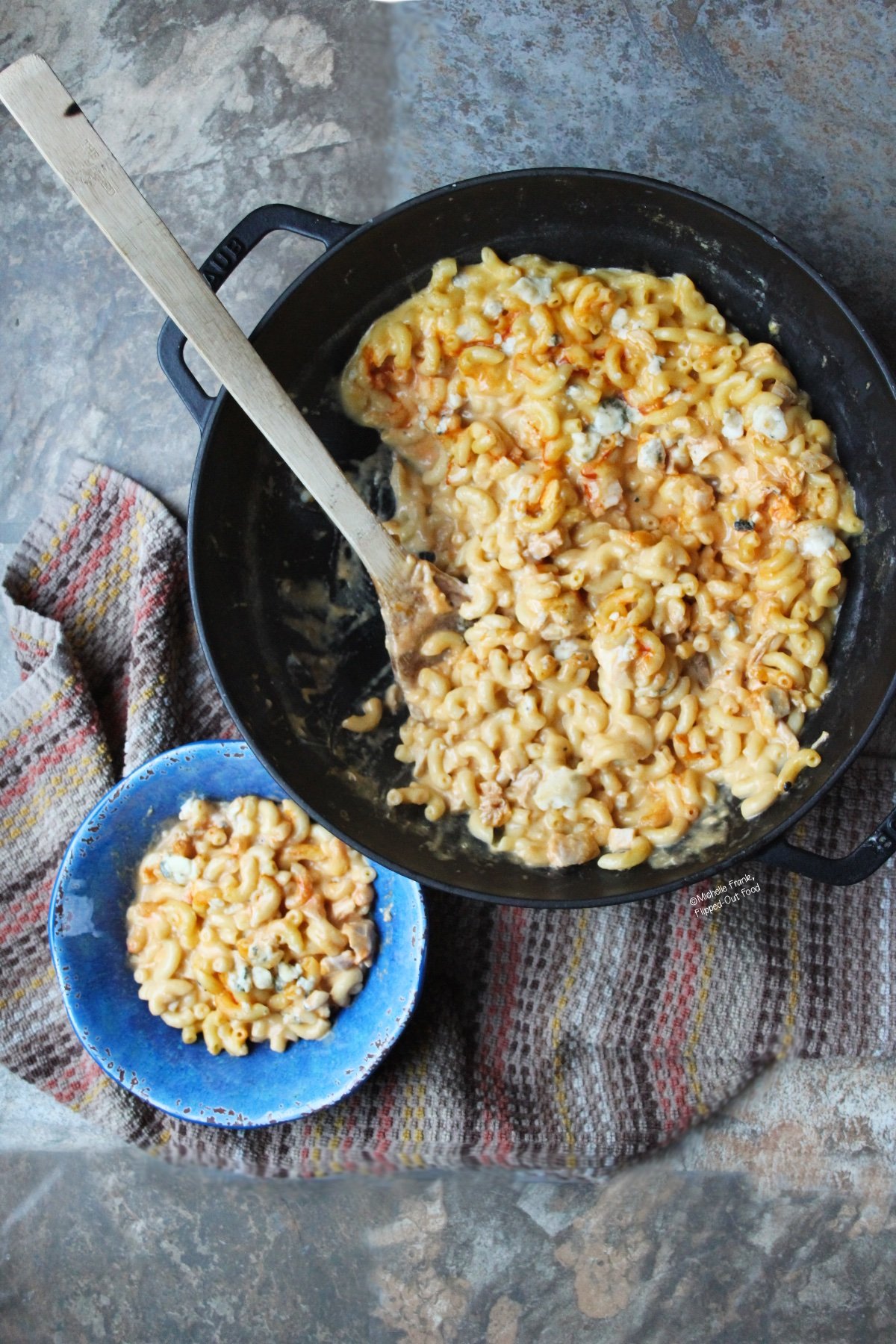 One-Pot Buffalo Chicken Macaroni and Cheese: top view showing a single serving in a blue bowl next to the skillet full of macaroni and cheese.