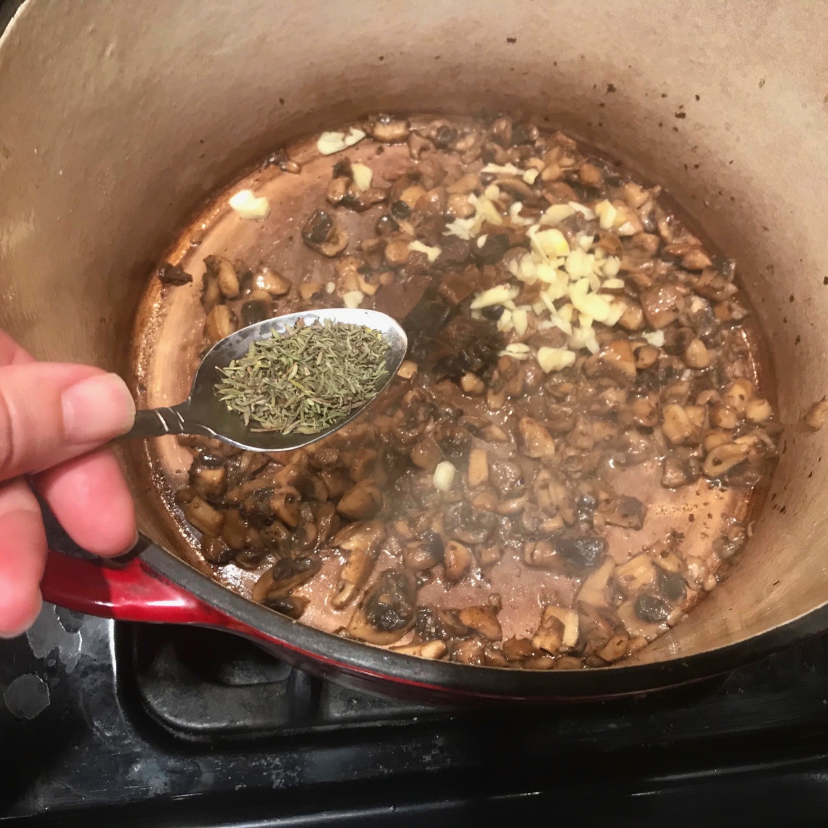 Adding thyme and garlic to the mushrooms in the pot.