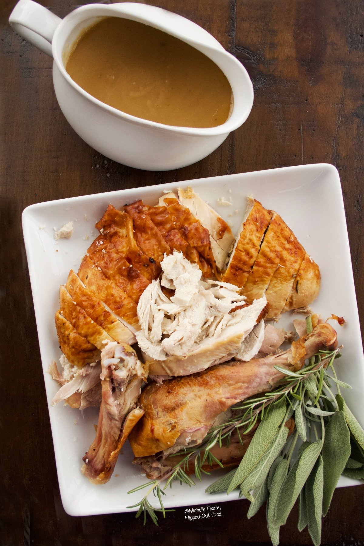 Easy Turkey Gravy in a white, porcelain gravy boat sitting next to a platter of sliced turkey garnished with sage.