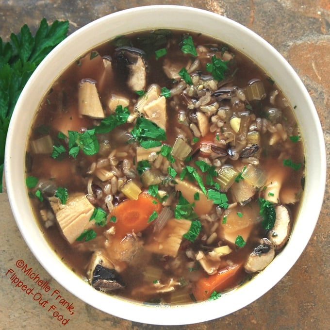 Top view of a white, ceramic bowl full of turkey wild rice soup. Parsley is sprinkled over the top, and a sprig of parsley sits next to the bowl.