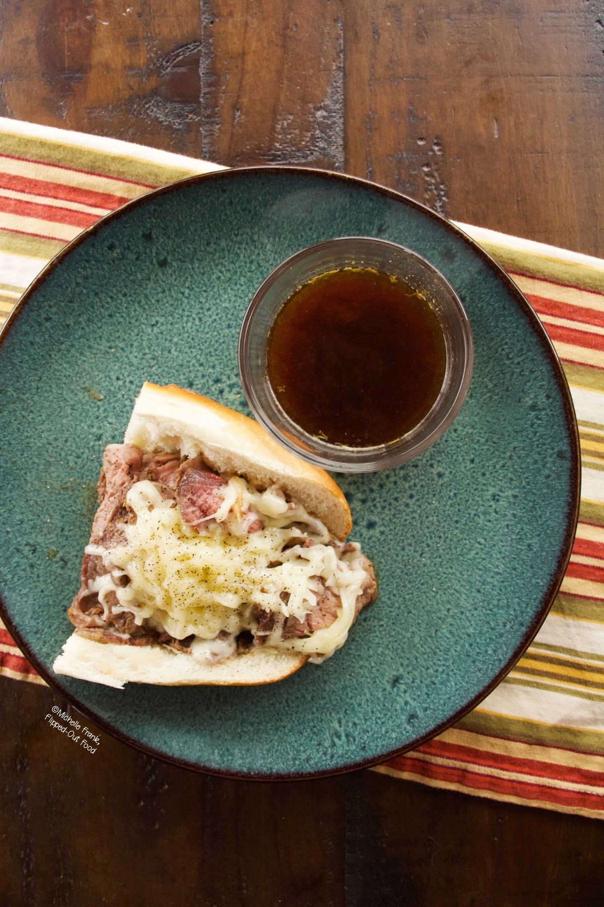 overhead view of Prime Rib Sandwich on a ceramic plate with a ramekin of au jus.