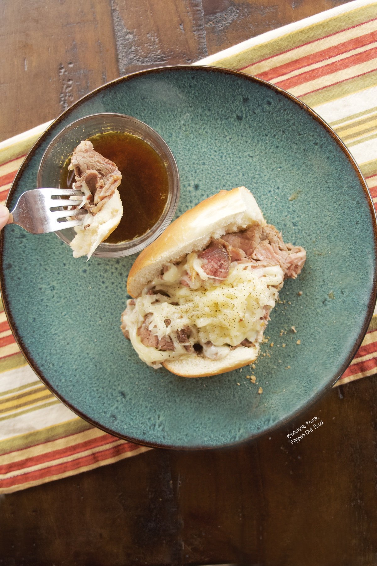 Overhead view of an Open-Faced Prime Rib Sandwich with a slice of sandwich on a fork, about to be dipped into a ramekin of au jus.