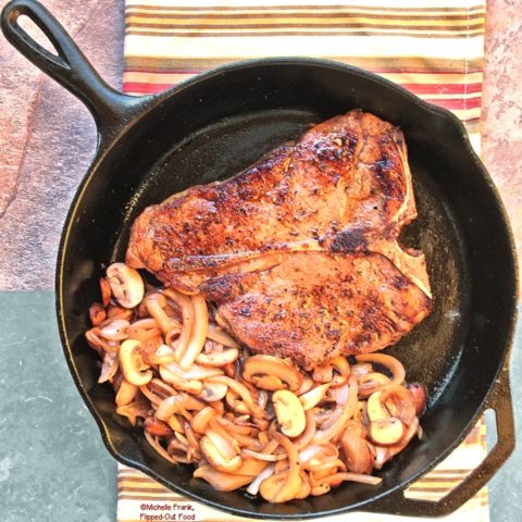 Steak Mushroom Onion Skillet: a porterhouse steak in a cast-iron skillet with caramelized mushrooms and onions. The skillet sits atop a colorful striped cloth.