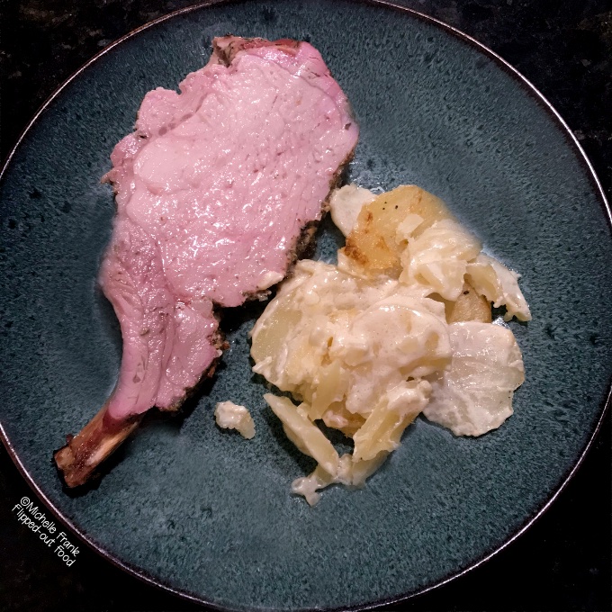 A single chop of Herb-Roasted Rack of Pork served alongside scalloped potatoes on a blue plate.