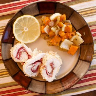 Work-Ahead Chicken Rollatini sliced on a ceramic plate with roasted vegetables and a slice of lemon.