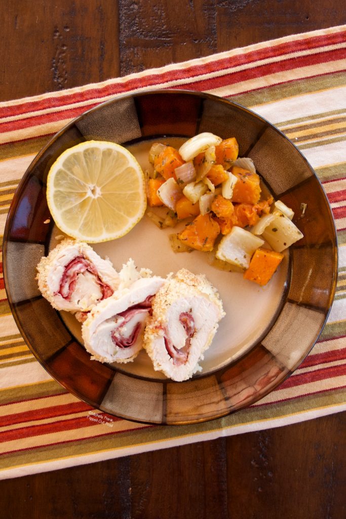 Work-Ahead Chicken Rollatini sliced on a ceramic plate with roasted vegetables and a slice of lemon.