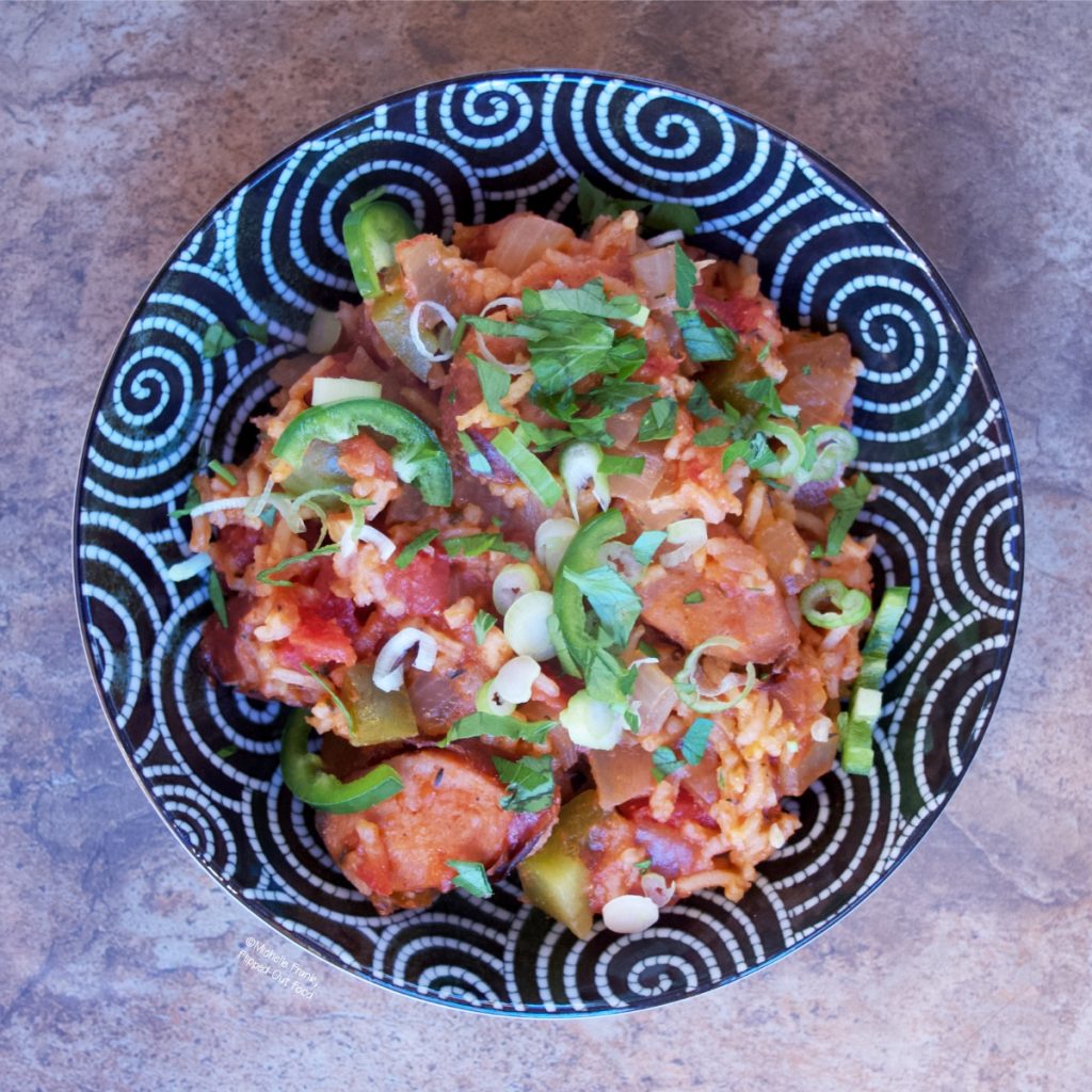 A bowl with a serving of Cajun Sausage-Rice Skillet, garnished with parsley, scallions, jalapenos, and hot sauce. Yep, we like it hot in this house!