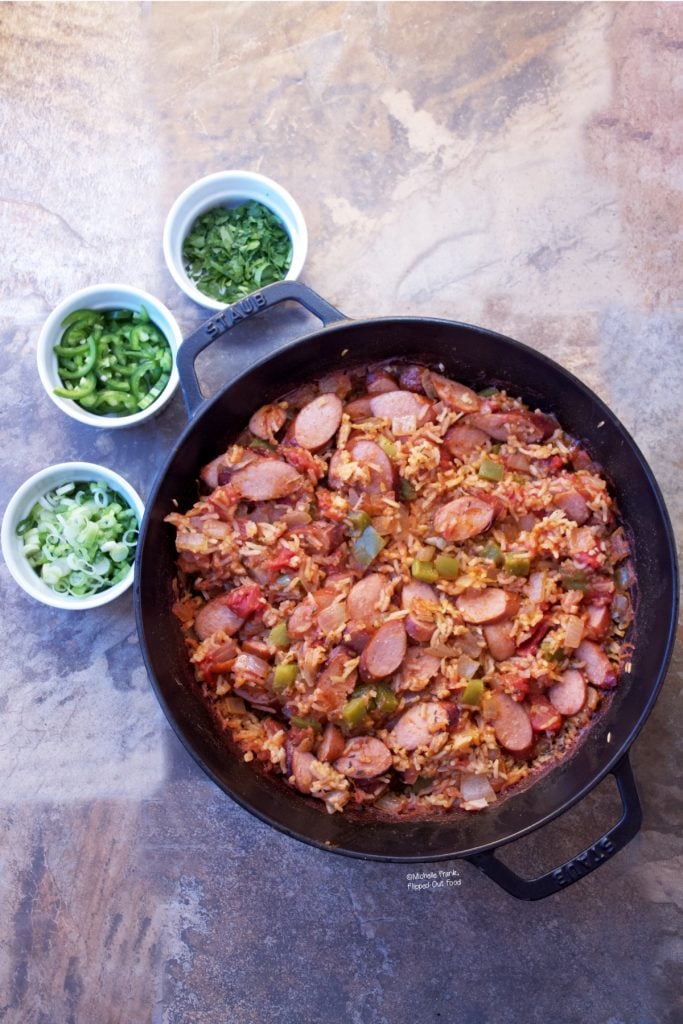 The finished Cajun Sausage-Rice Skillet, ready to serve, sitting next to ramekins of scallions, jalapenos, and parsley.