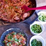 Cajun Sausage Rice Skillet with a serving dished out into a bowl in the foreground. Ramekins with scallions, jalapenos, and parsley sit to the side.