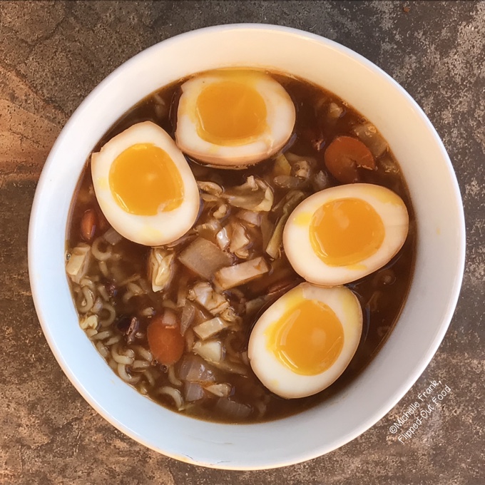 A bowl of ramen soup with 2 soy-miso marinated eggs, sliced in half, floating in the broth.